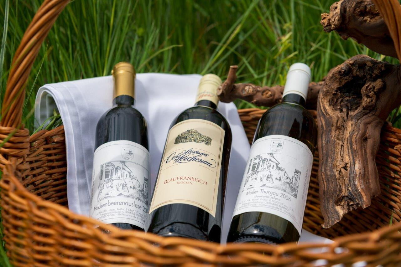 Three bottles of wine lying in a basket in the countryside.