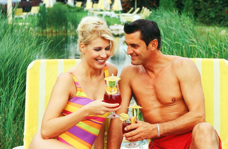 Ein Mann und eine Frau im Badeanzug mit Cocktails in der Hand am Pool im Hotel Das-Schmidt