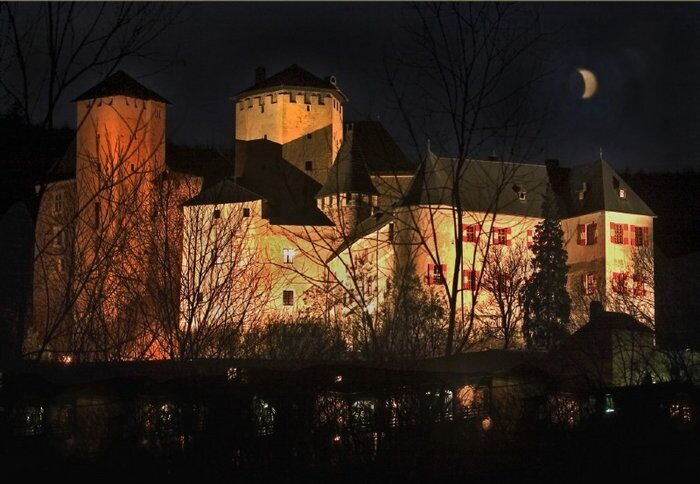 Nachts beleuchtete Burg Lockenhaus mit einem Halbmond im Hintergrund