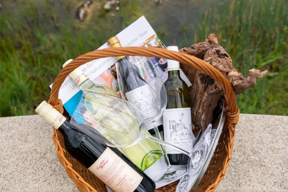 A few bottles of wine and two wine glasses in a woven basket at Hotel Das-Schmidt in Burgenland